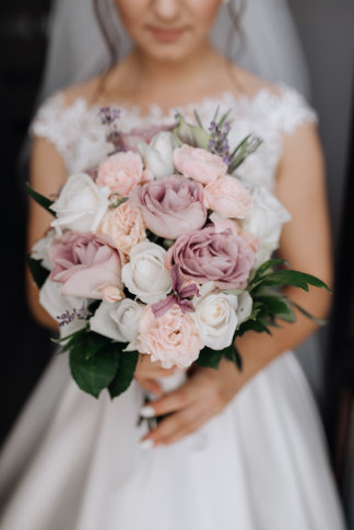 A bride, dressed in white, holds a bouquet of pink and white roses from a Floral Design Company in Sacramento.